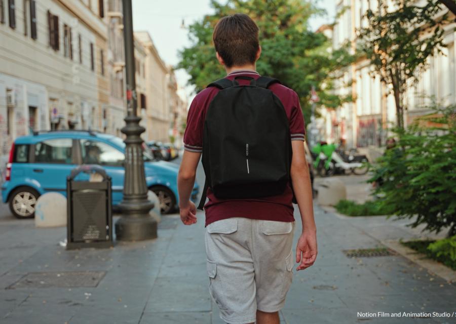 Adolescente con zaino in spalla cammina di spalle su un marciapiede