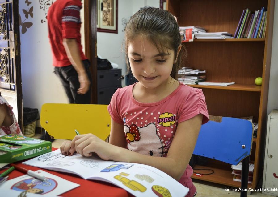 Bambina con maglietta rosa di hello kitty è seduta a un tavolino e guarda un libro mentre lo sfoglia.
