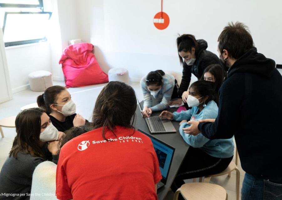 ragazzi e ragazze guidate da operatore save the children mentre lavorano in gruppo al computer