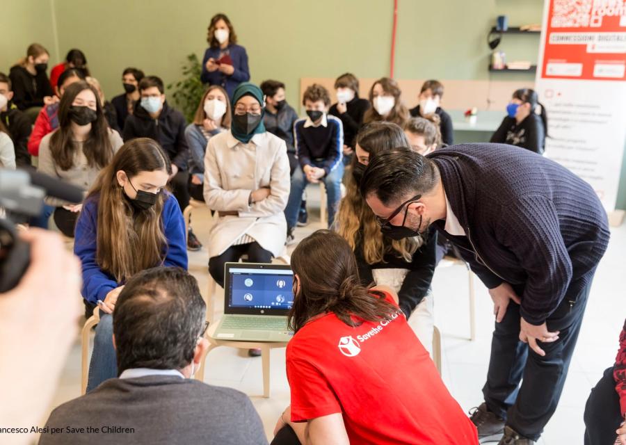 in una classe di studenti quattro persone sono sedute attorno ad un pc e lo guardano. Una è operatrice save the children