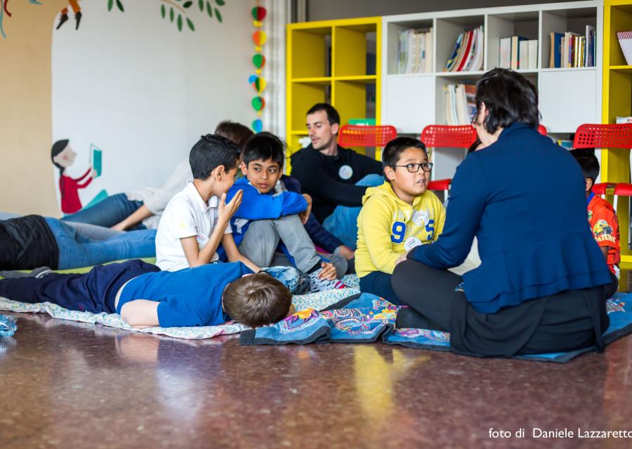 bambini seduti a terra che giocano insieme ad un insegnante dopo il rientro a scuola