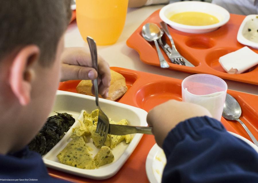 bambino di spalle mentre mangia in un piatto da mensa scolastica