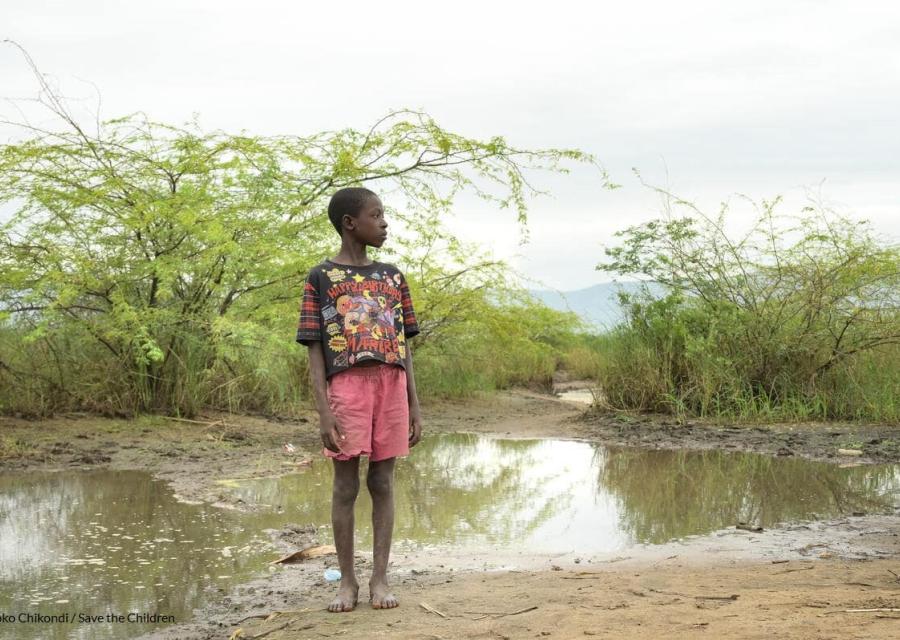 bambino a piedi nudi su un terreno fangoso dopo inondazione a causa della crisi climatica