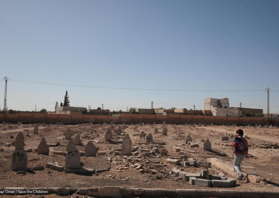 bambino in siria con zaino in spalla che cammina su un terreno distrutto dalla guerra