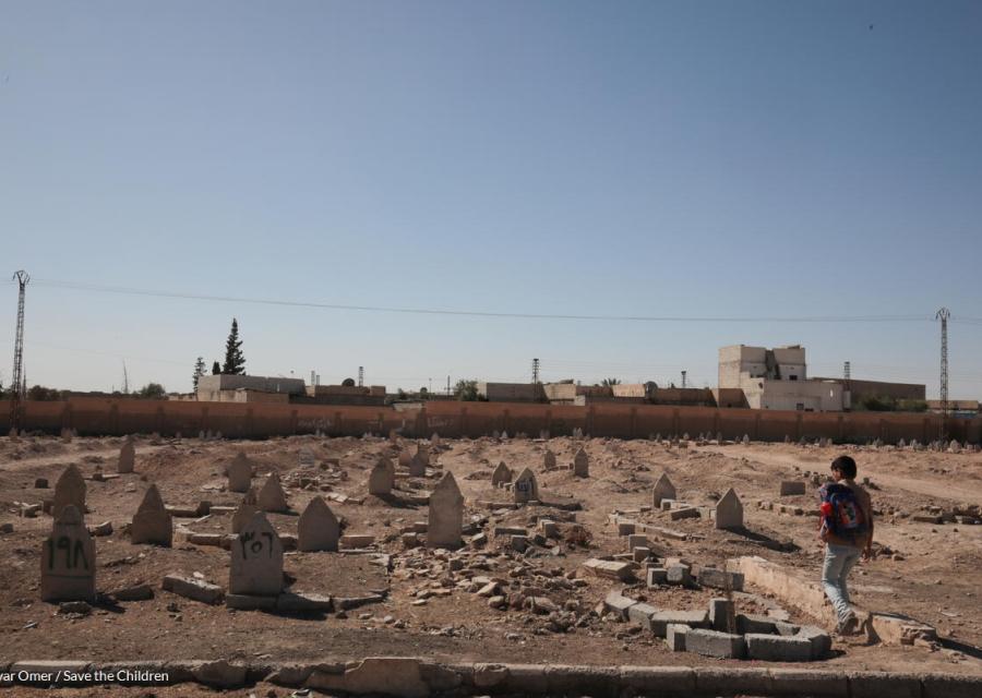 bambino in siria con zaino in spalla che cammina su un terreno distrutto dalla guerra