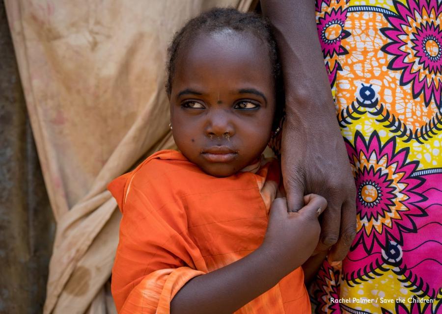 Primo piano di una bambina nigeriana con indosso una maglietta arancione che tiene per mano la mamma