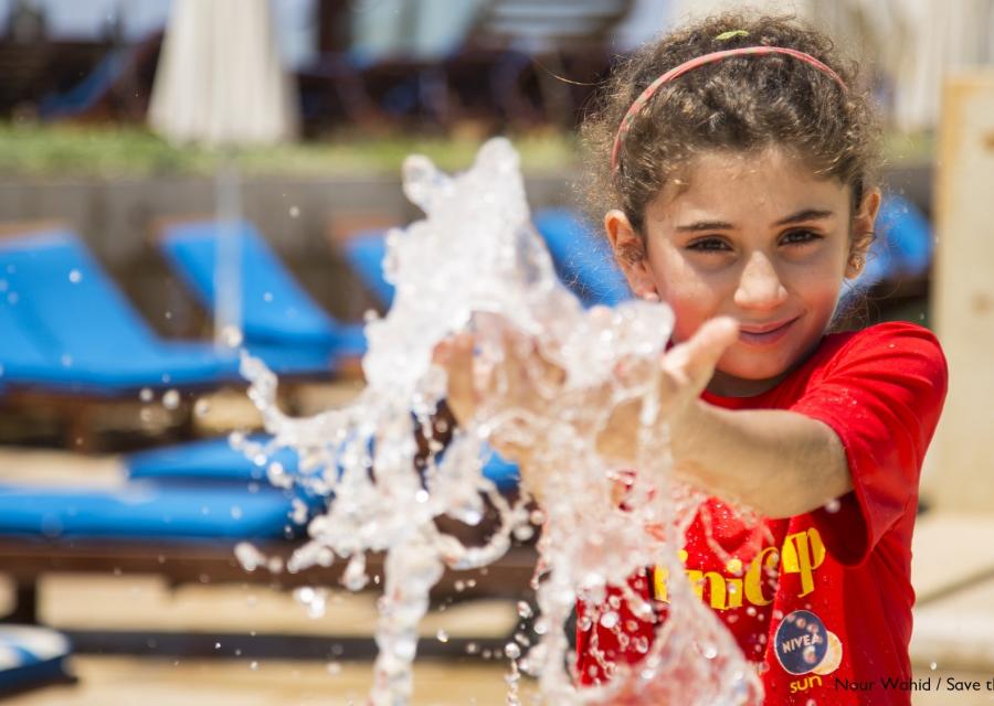bambina bianca in primo piano con le mani tra lo spruzzo di una fontana