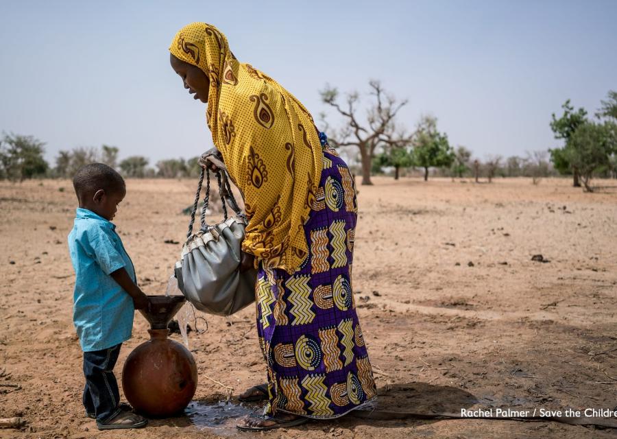Campo lungo di madre e figlio nigeriani che si riforniscono di acqua in una terra brulla