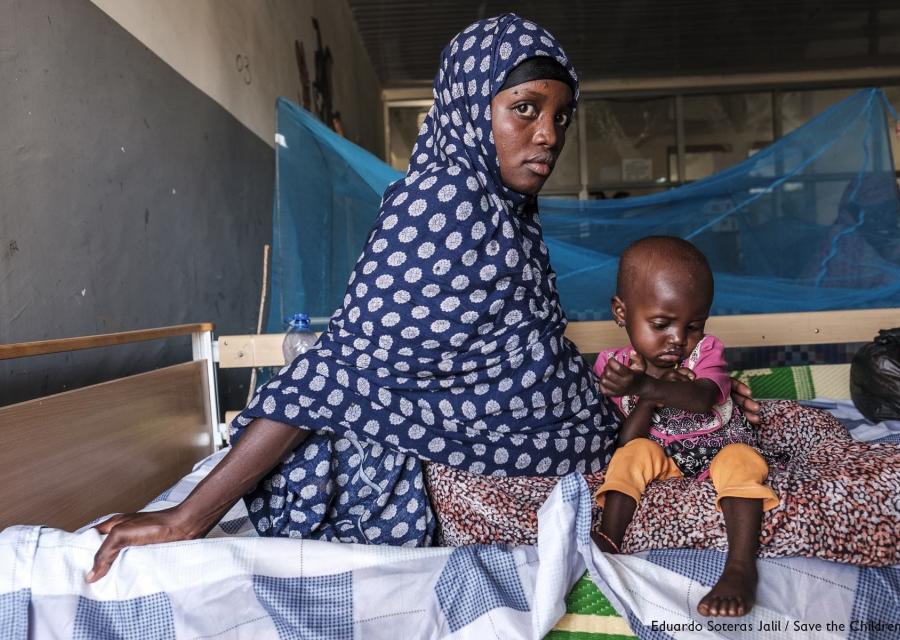 Mamma africana tiene in braccio bambino malnutrito entrambi sono seduto sul letto di una clinica