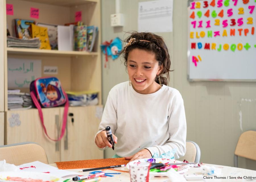 ragazza seduta a un tavolo fa lavori con carta, forbici e colori