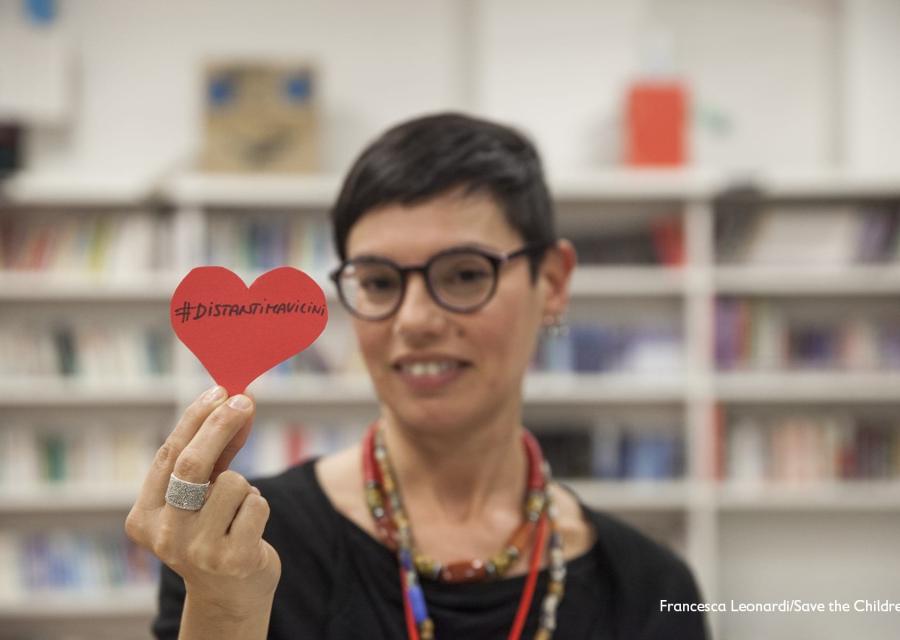donna con capelli corti tiene in mane un cuore di carta con scritta #distantimavicini