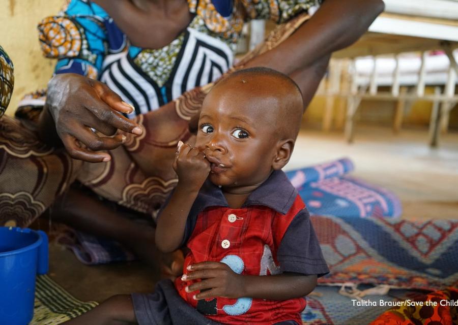 bambino nigeriano seduto a terra su un telo mangia plumpynut