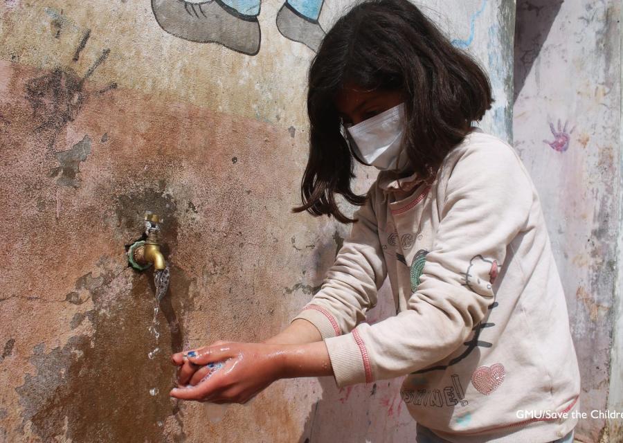 Bambina siriana con mascherina in volto si lava le mani a una fontana