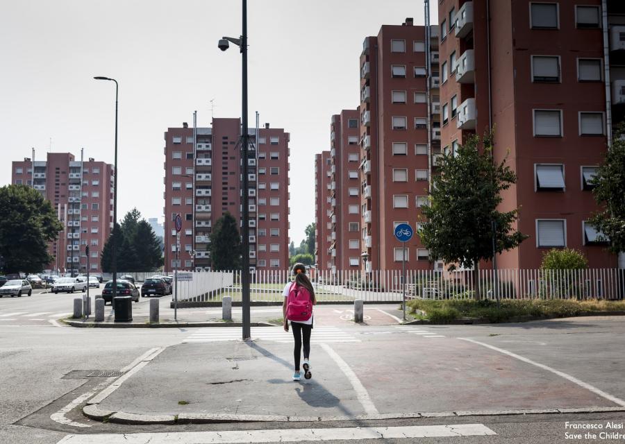 bambina di spalle cammina lungo una strada deserta a Milano tra i palazzi