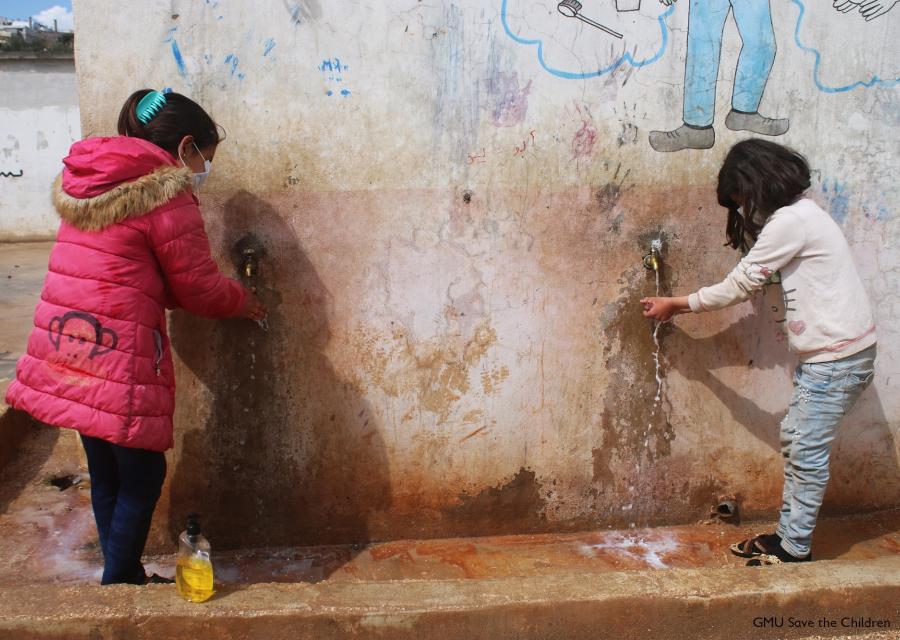 due bambine con mascherina in piedi davanti a un muro mentre si lavano le mani