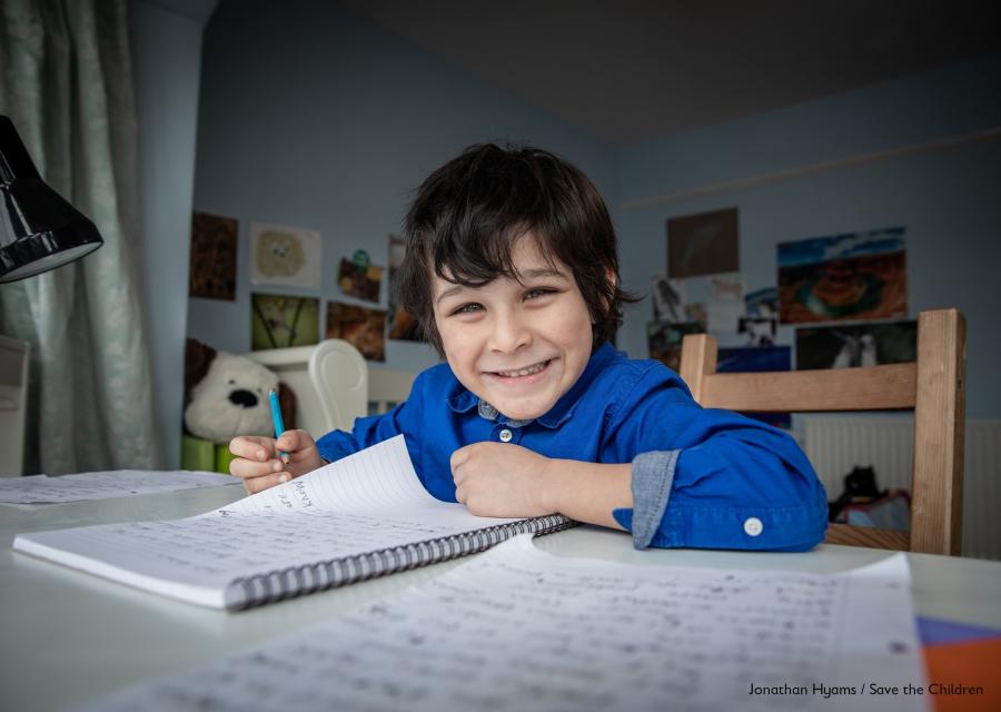 Bambino inglese seduto alla sua scrivania della camera mentre scrive su un quaderno