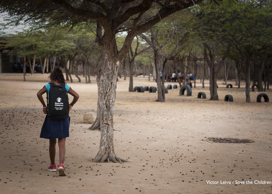 bambina di spalle con lo zaino cammina su terreno vicino a un albero