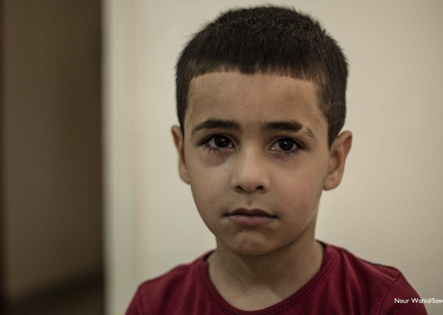 Primo piano ritratto di un bambino di circa sei anni libanese. Ha capelli corti, occhi e capelli bruni. Indossa una maglietta rossa