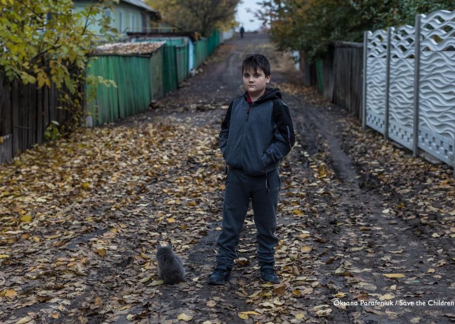 bambino ucraino posa in piedi su una strada ricoperta di foglie 