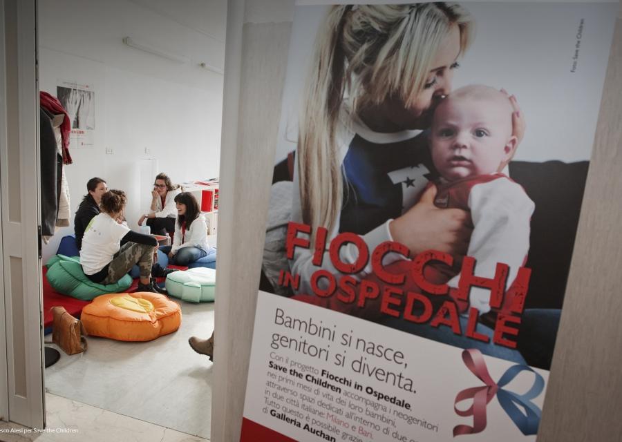 sulla parete destra lo  striscione di Fiocchi in Ospedale con madre e figlio abbracciati, nella parte sinistra della foto 4 donne che parlano e ridono