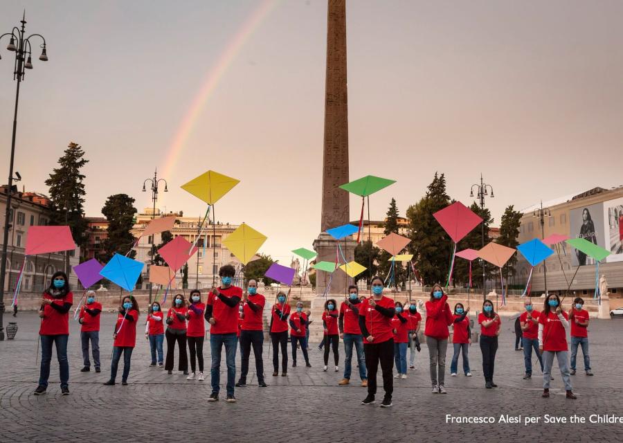 persone con maglietta rossa azione con aquiloni a roma davanti ad un arcobaleno