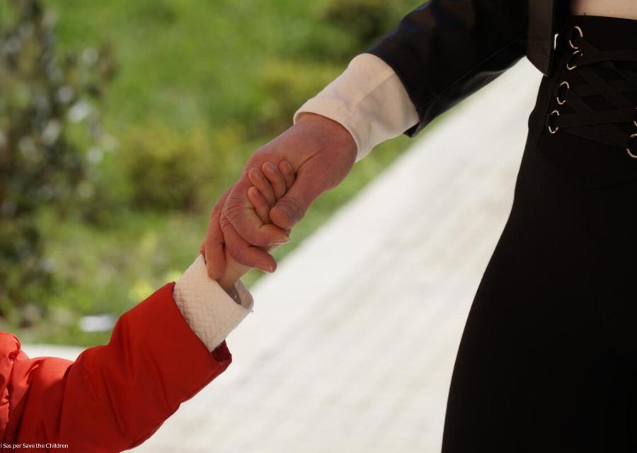 mano di un bambino con la magglietta rossa che si unisce alla mano della madre con maglietta nera su sfondo di un giardino