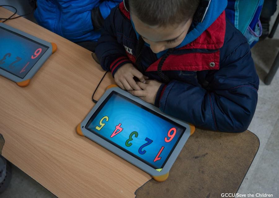 bambino seduto al banco studia con un tablet davanti