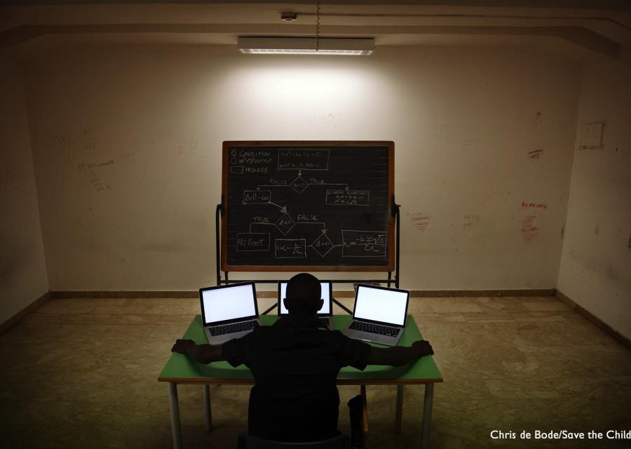 Ragazzo di spalle seduto al tavolo con tre computer