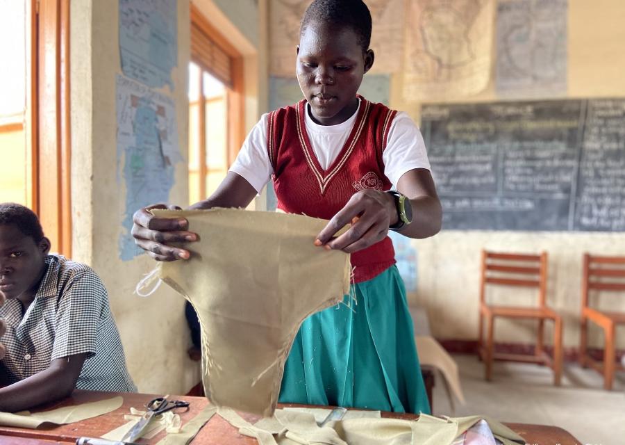 Ragazza ugandese in divisa scolastica tiene in mano slip autoprodotti.