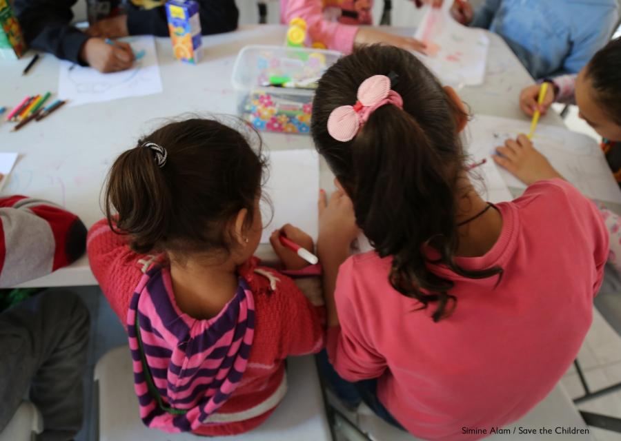 due bambine di spalle al banco di scuola che disegnano