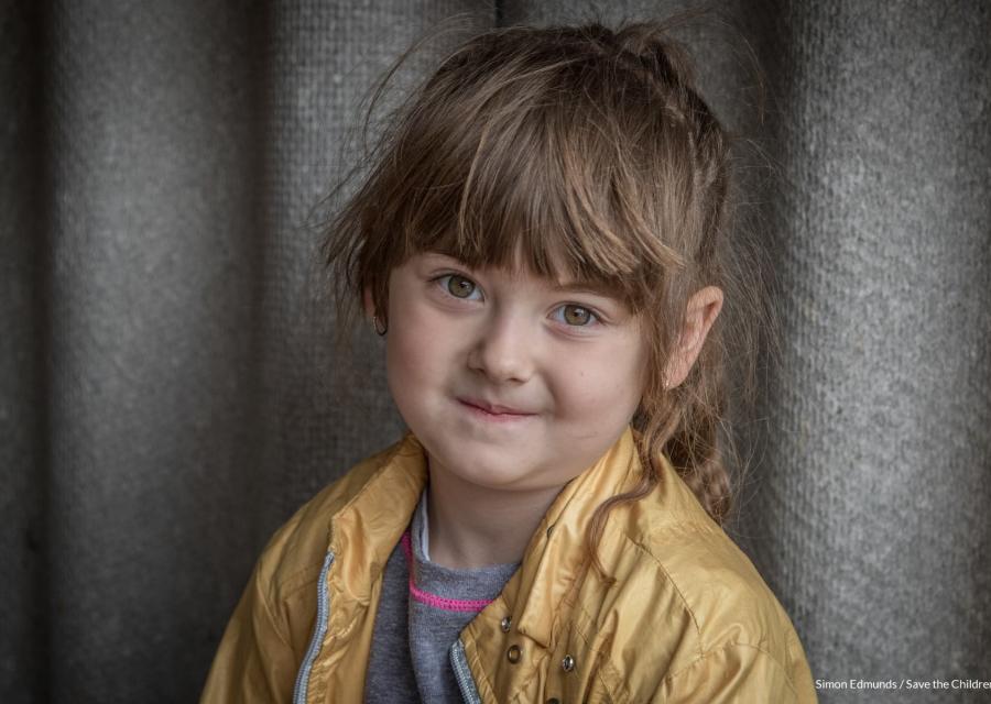 primo piano di bambina sorridente bionda con la coda sorridente. Indossa una giacca gialla e una maglietta celeste