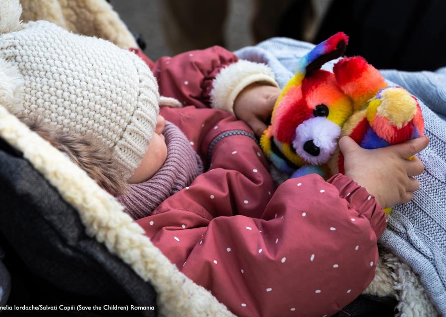 bimba nel passeggino con giacchina rosa tiene un peluches tutto colorato