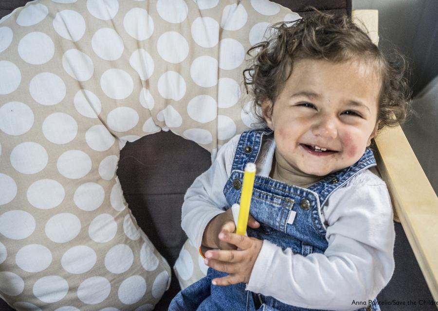 bambina bianca con i capelli ricci seduta con in mano un pennarello giallo