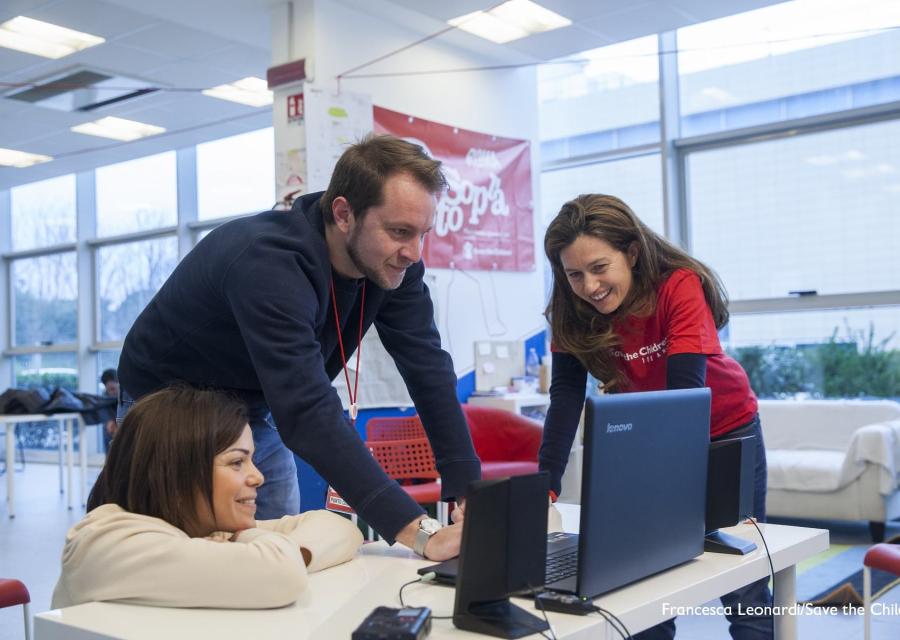 Tre operatori Save the Children guardano un pc appoggiato su un tavolo