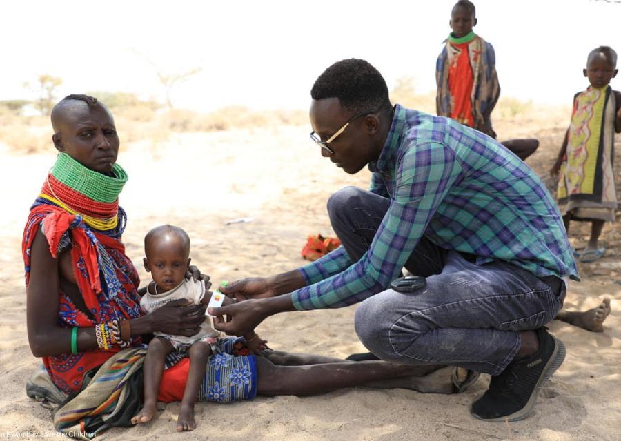 Bambino keniota in braccio alla madre mentre un dottore misura il livello di malnutrizione mettendo il braccialetto MUAC  attorno al braccio 