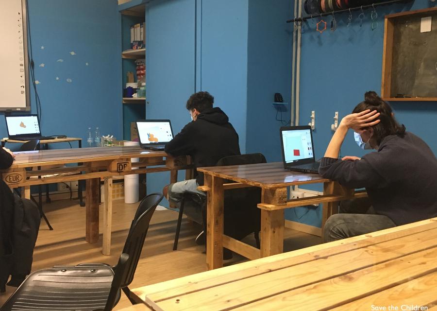 Stanza con tavoli di legno a cui sono seduti due ragazzi adolescenti al computer e ripresi di spalle. Indossano entrambi felpe di colore scuro.