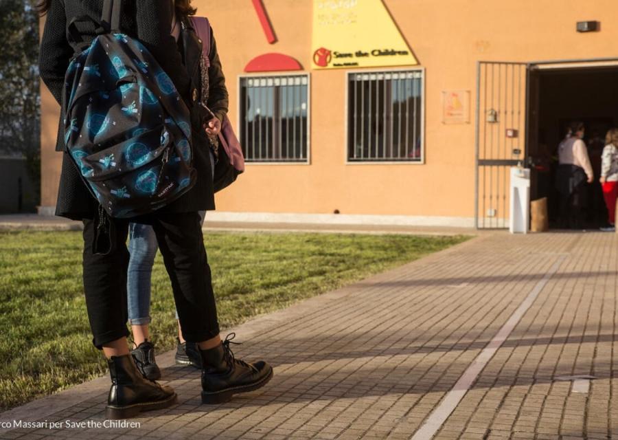 Ragazzi con lo zaino in spalla nel cortile di fronte la porta d'ingresso della scuola