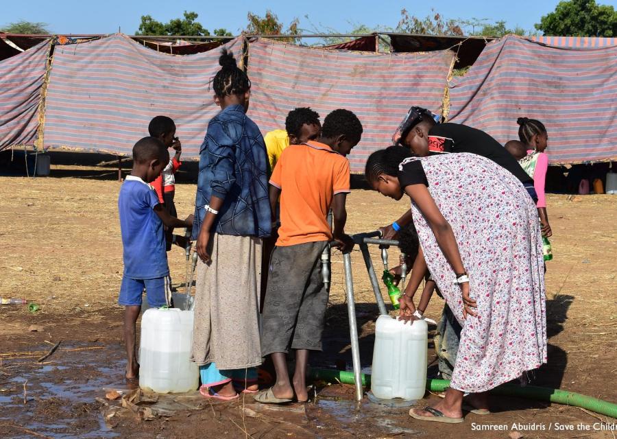 un gruppo di bambini e ragazzi etiopi in un campo per rifugiati si affollano intorno a una fonte d'acqua per raccoglierla con le taniche