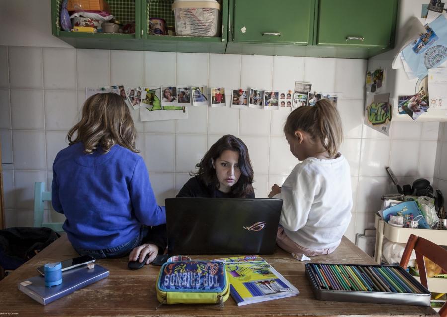 mamma che lavora al pc mentre le due figlie sono sedute sul tavolo accanto a lei 