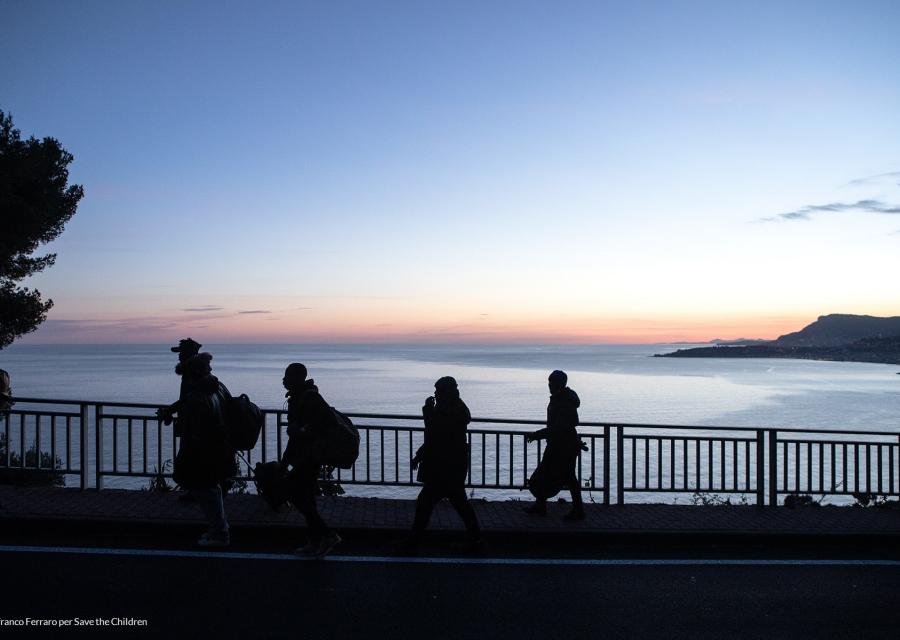 Quattro sagome in controluce affacciate da una ringhiera sul mare al tramonto
