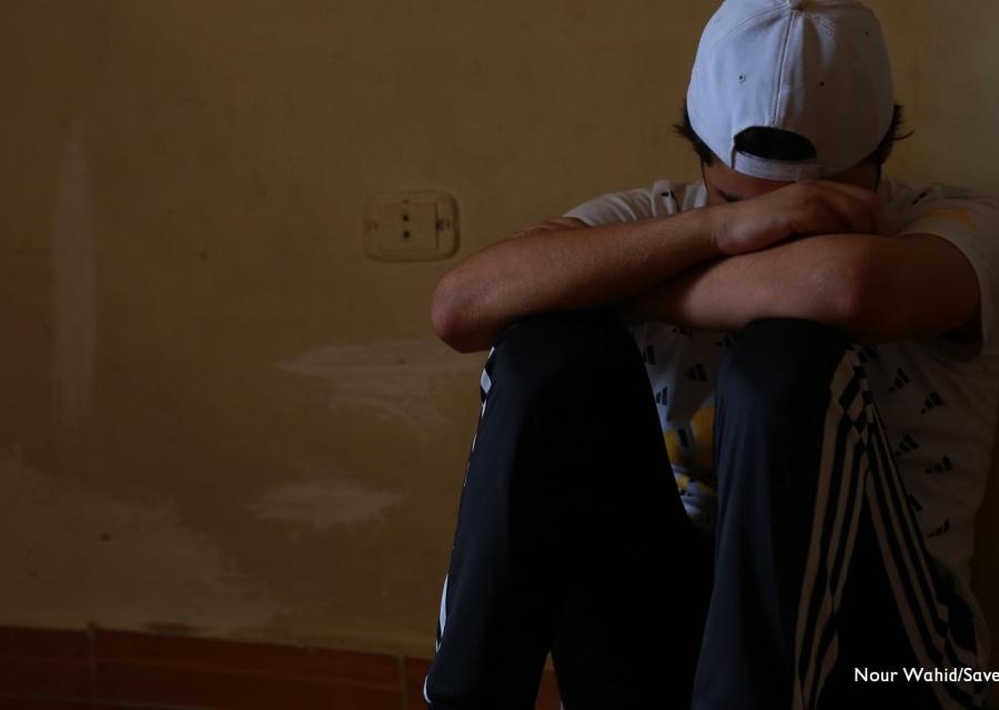 Un ragazzo rifugiato siriano seduto a terra appoggia la testa al braccio e la schiena al muro