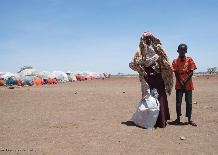 Madre e figlio fuori da un campo profughi in Somalia su terra arida con un sacco di yuta bianco