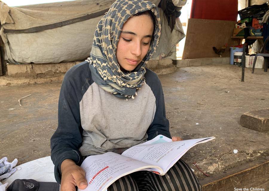 Ragazza palestinese con kufia in testa è seduta a terra e legge un quaderno che tiene poggiato sulle ginocchia