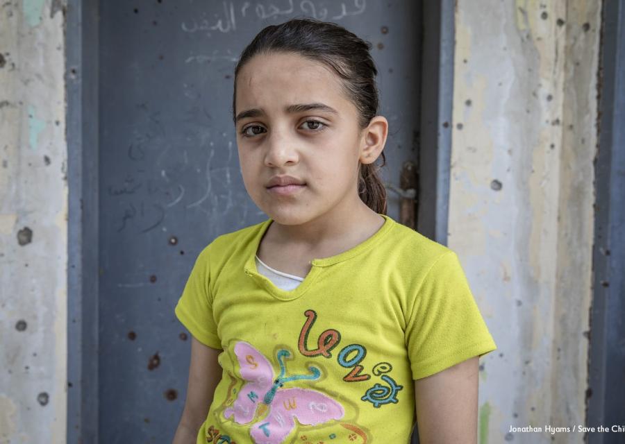 Mezzo busto di una bambina palestinese che indossa una maglietta gialla a maniche corte con alcune scritte colorate sopra. La bambina è castana ed ha i capelli raccolti in una coda.