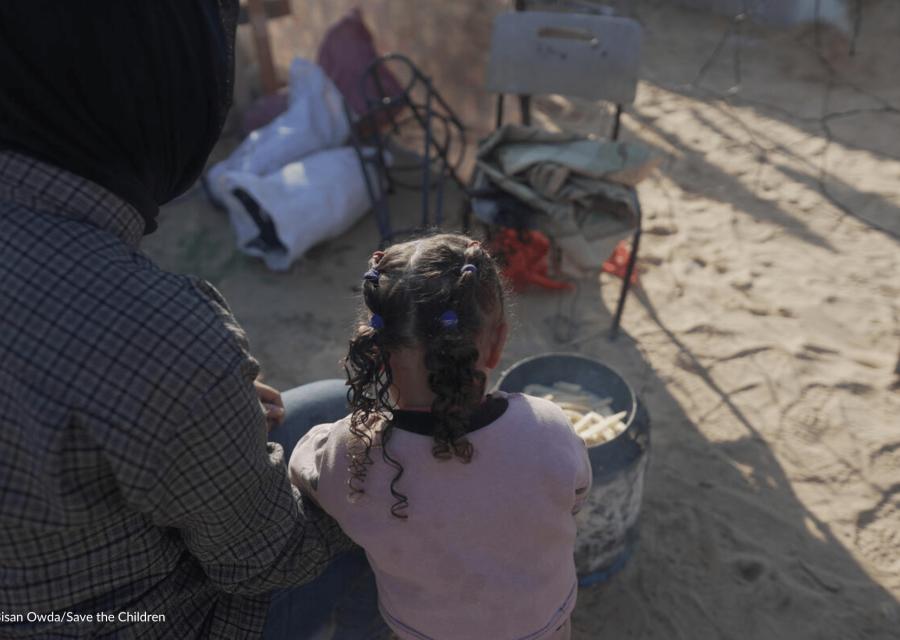 bambina a Gaza con accanto madre che guarda una pentola con cibo 