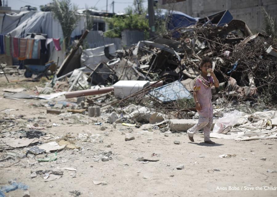 bambina palestinese cammina davanti a un cumulo di spazzatura.