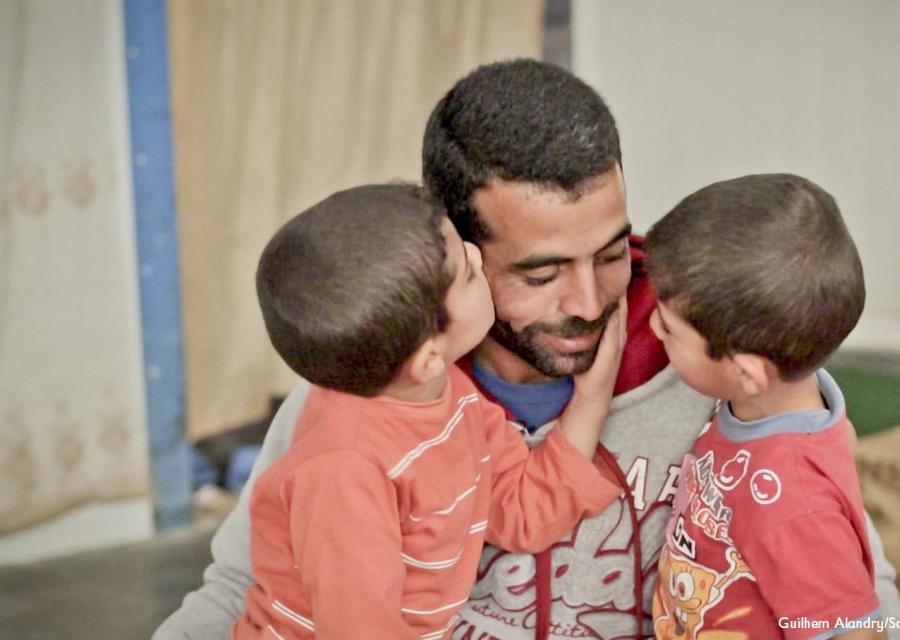 un papà chino sui figli, li abbraccia e uno dei due bambini gli accarezza la guancia e si avvicina per dargli un bacio