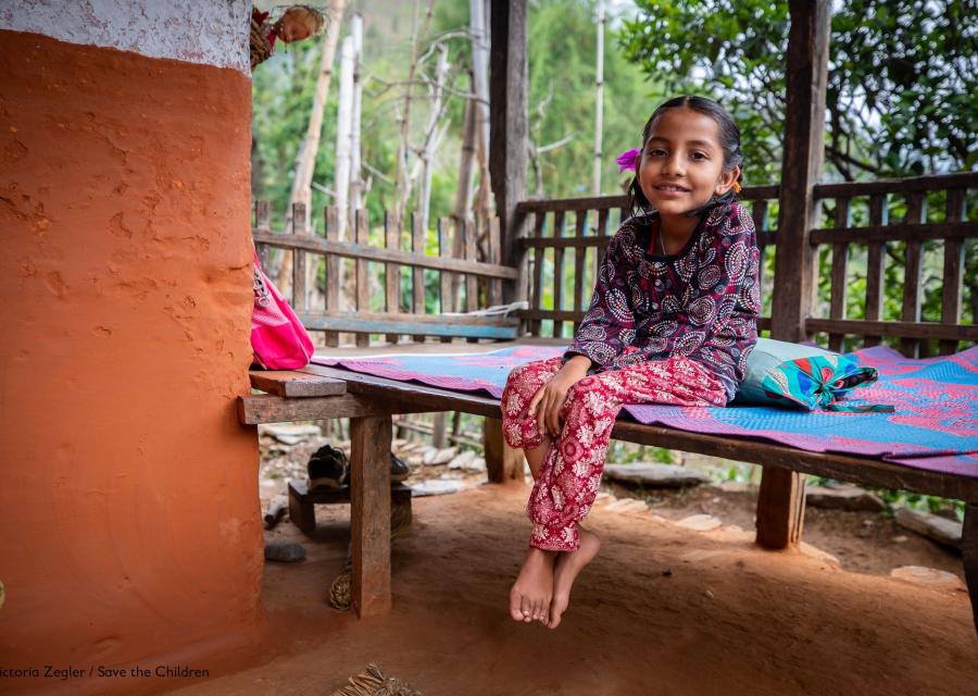 bambina seduta su un letto di legno in un patio vestita colorata con le treccine