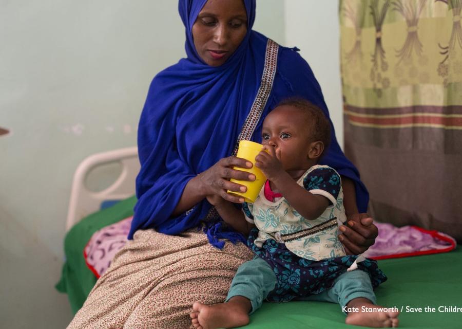 Mamma somala fa bere la figlia dal bicchiere sedute sul letto