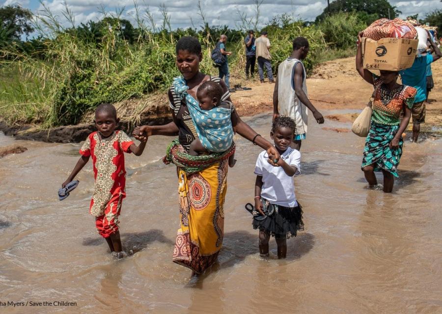 donna che tiene per mano i suoi bambini mentre attraversano un fiume